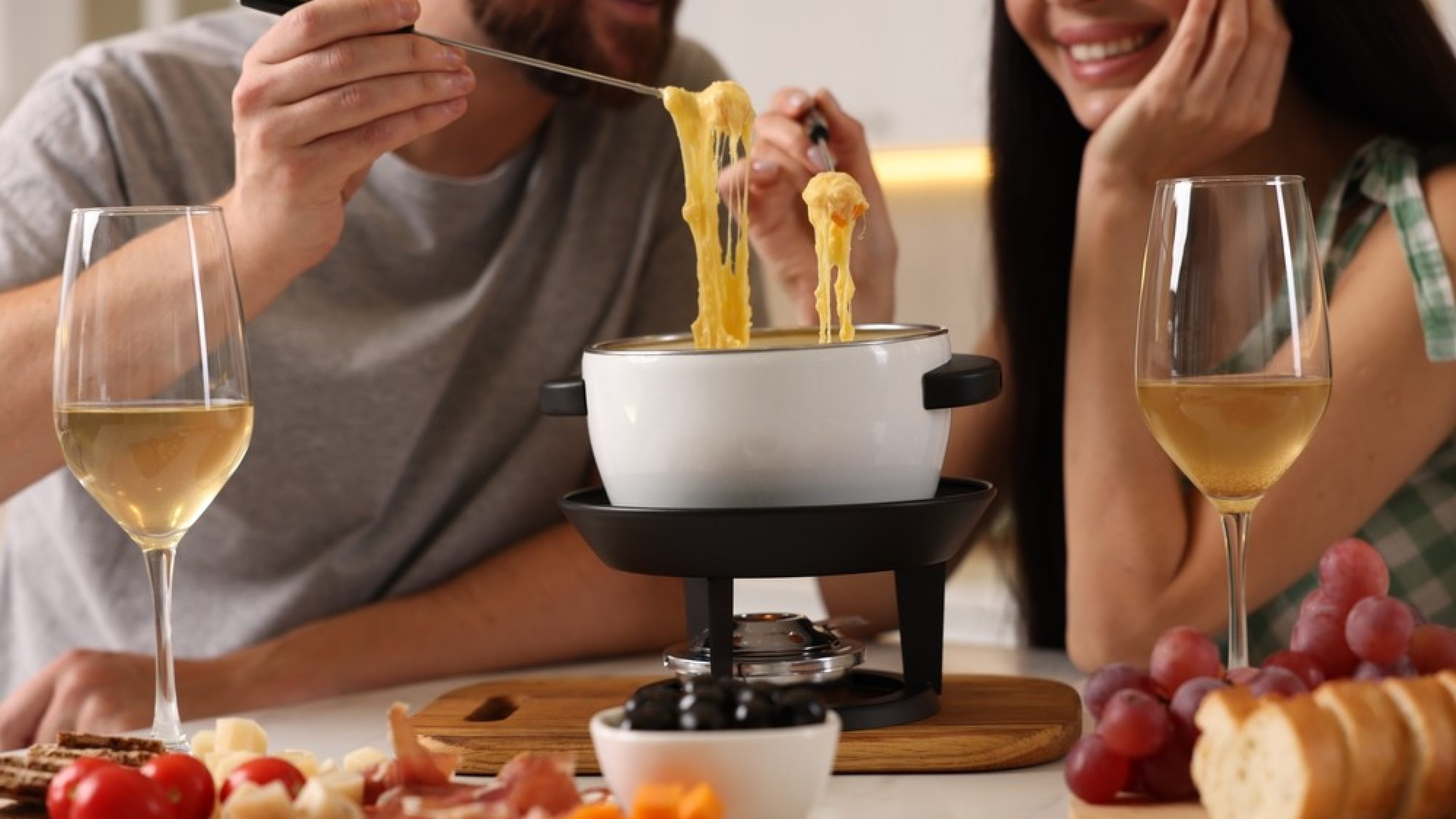 Couple enjoying cheese fondue during romantic date indoors, closeup