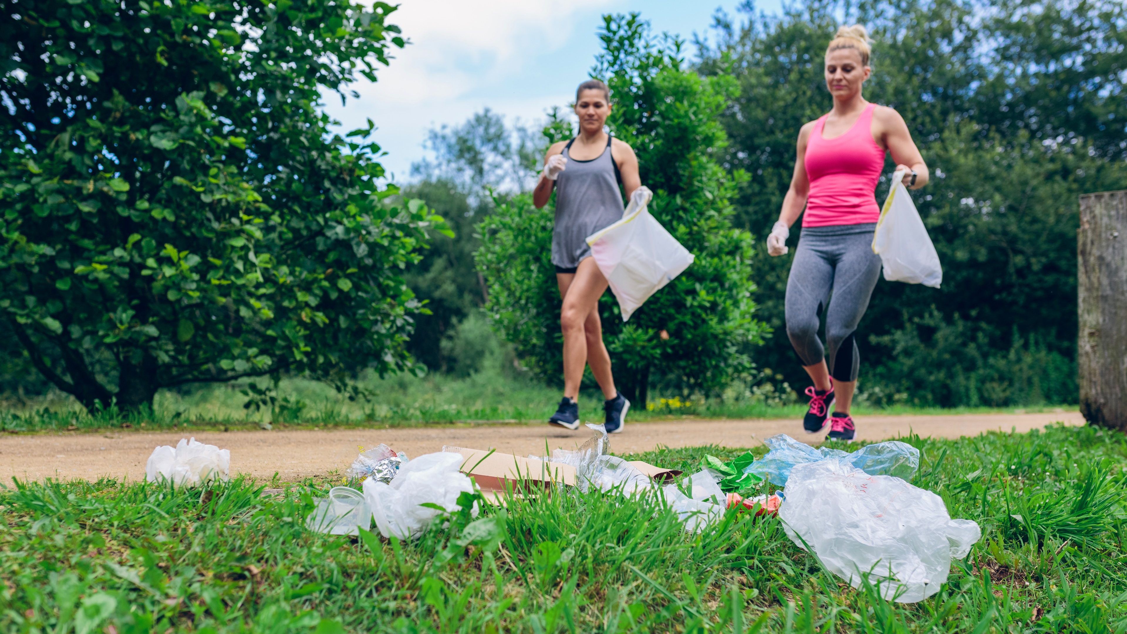 Waste pile and two girls running with bags doing plogging outdoors