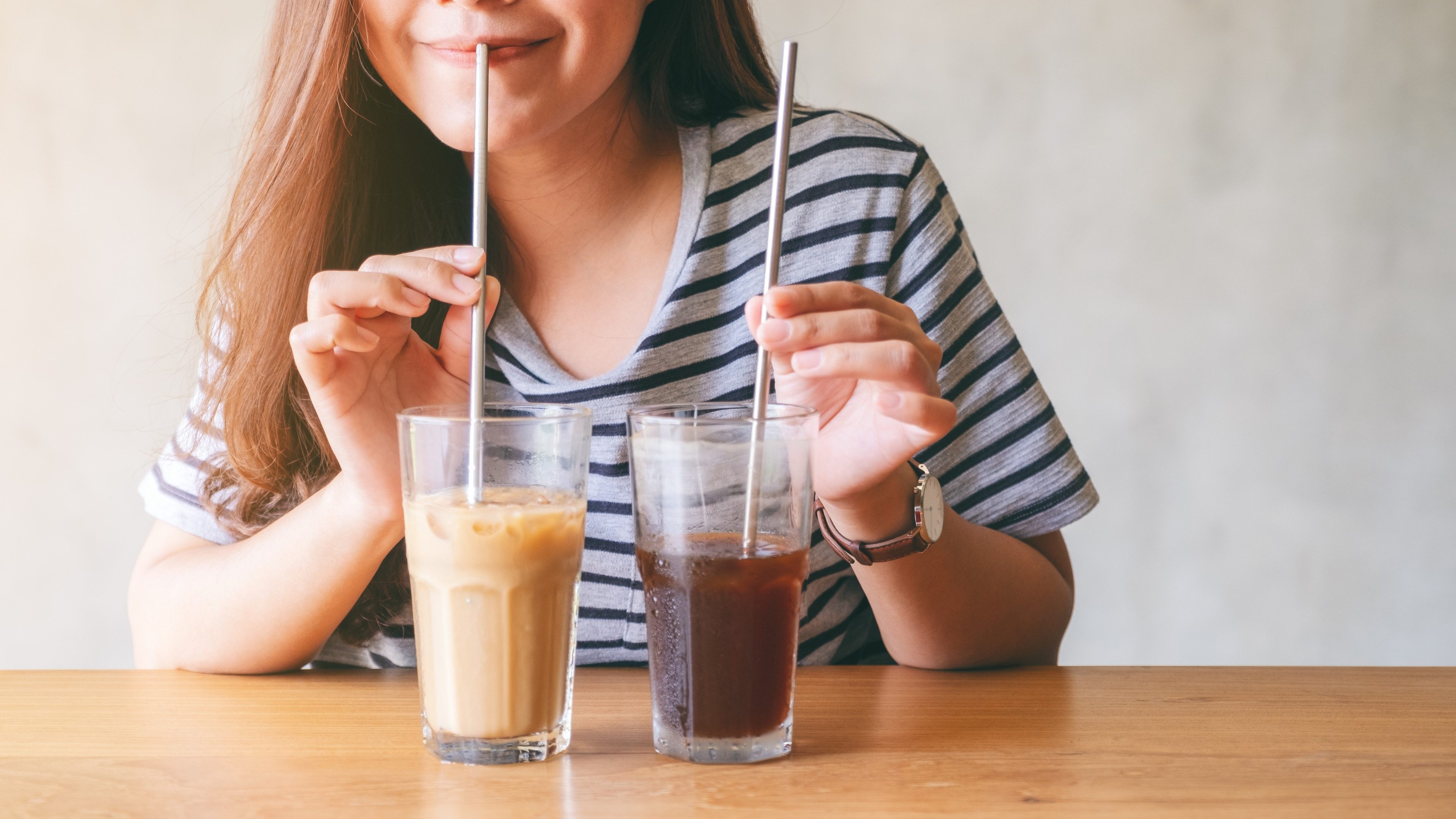 Closeup image of a beautiful asian woman drinking iced coffee with stainless steel straw 
