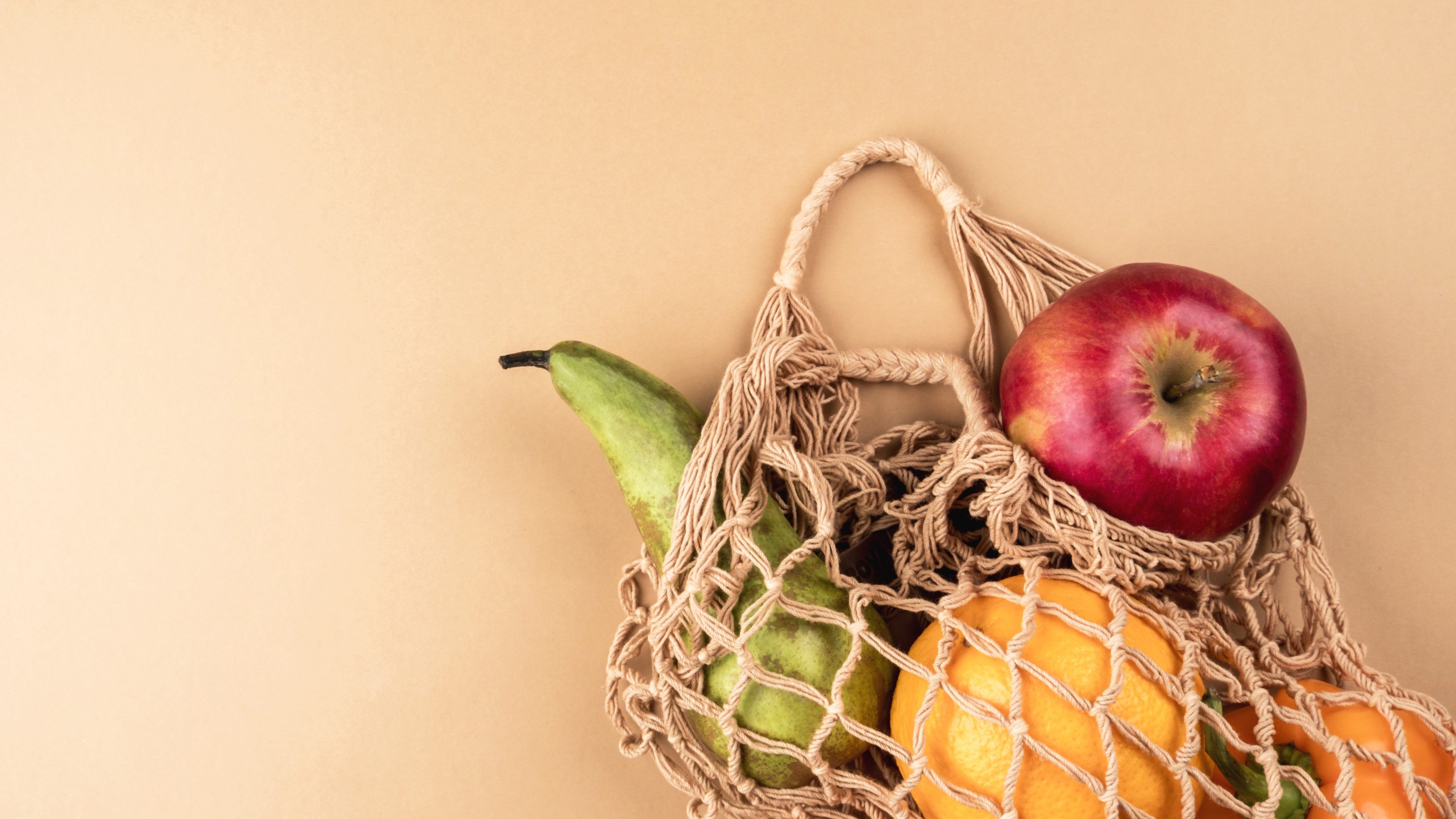 Fresh fruits and vegetables in a wicker eco-friendly bag on a beige background.  Zero waste