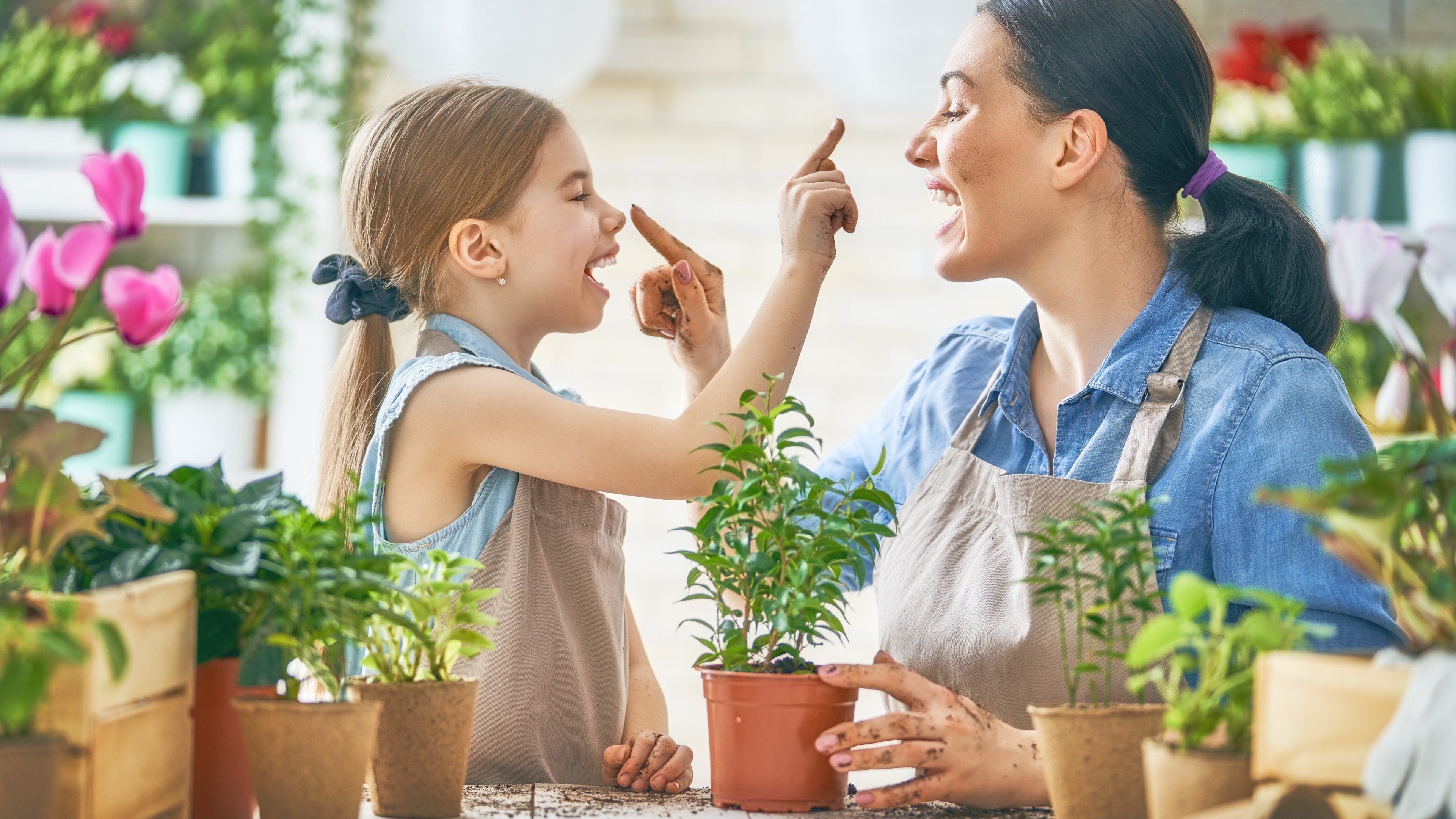 Cute child girl helping her mother to care for plants. Mom and her daughter engaging in gardening near window at home. Happy family in spring day.