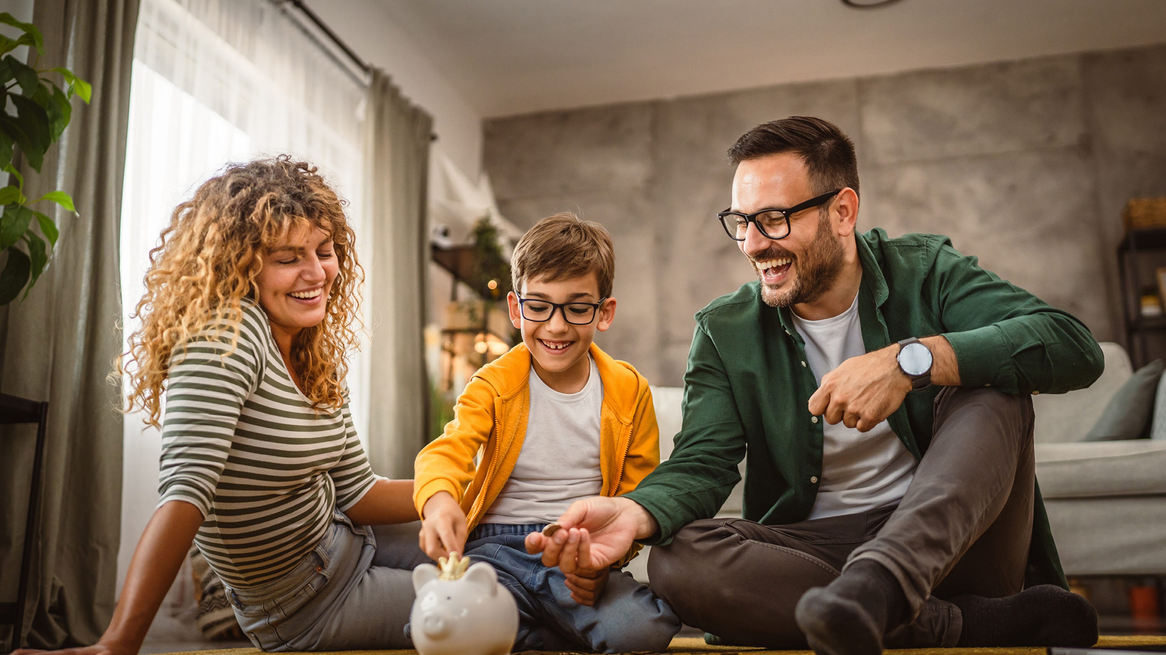 mam dad and son sit on the carpet,floor and save money in the piggy bank at home