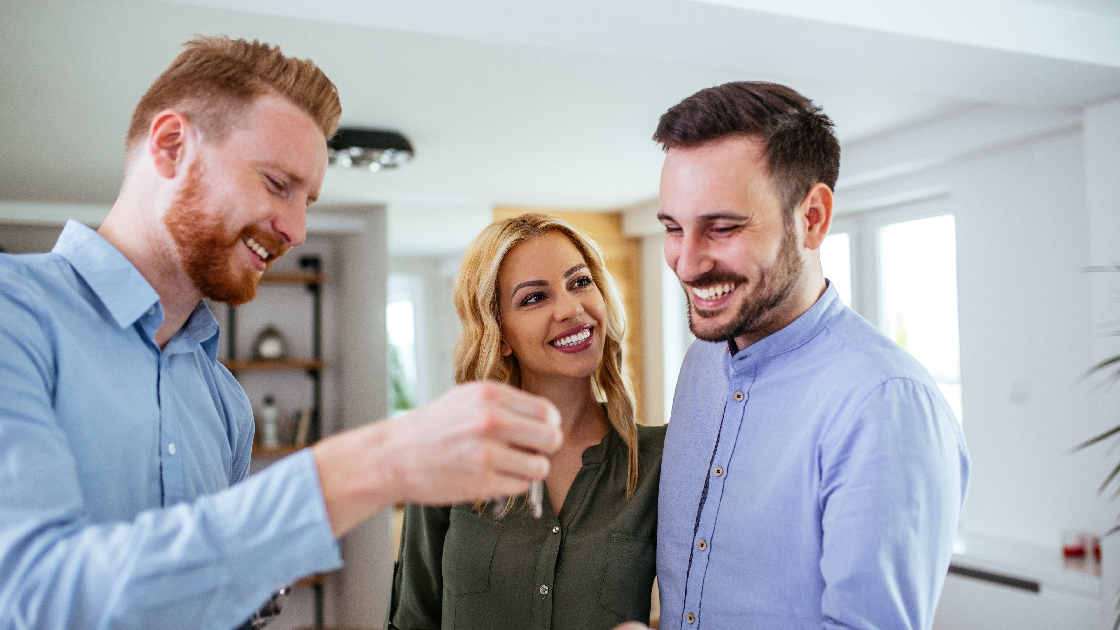 Lovely young couple buying a new house and receiving keys from consulting adviser.