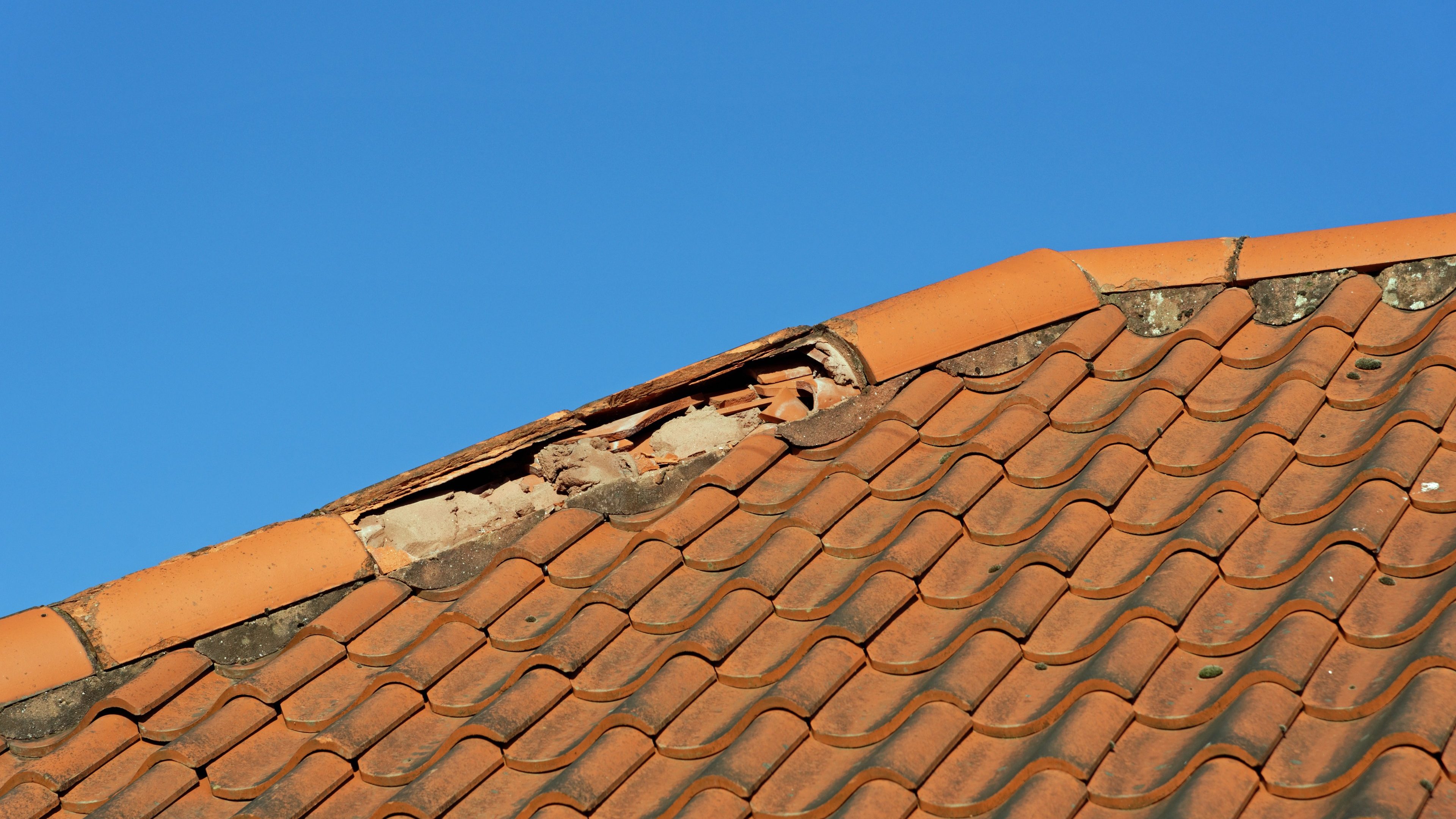 Damaged broken ridge roof tiles against a blue sky