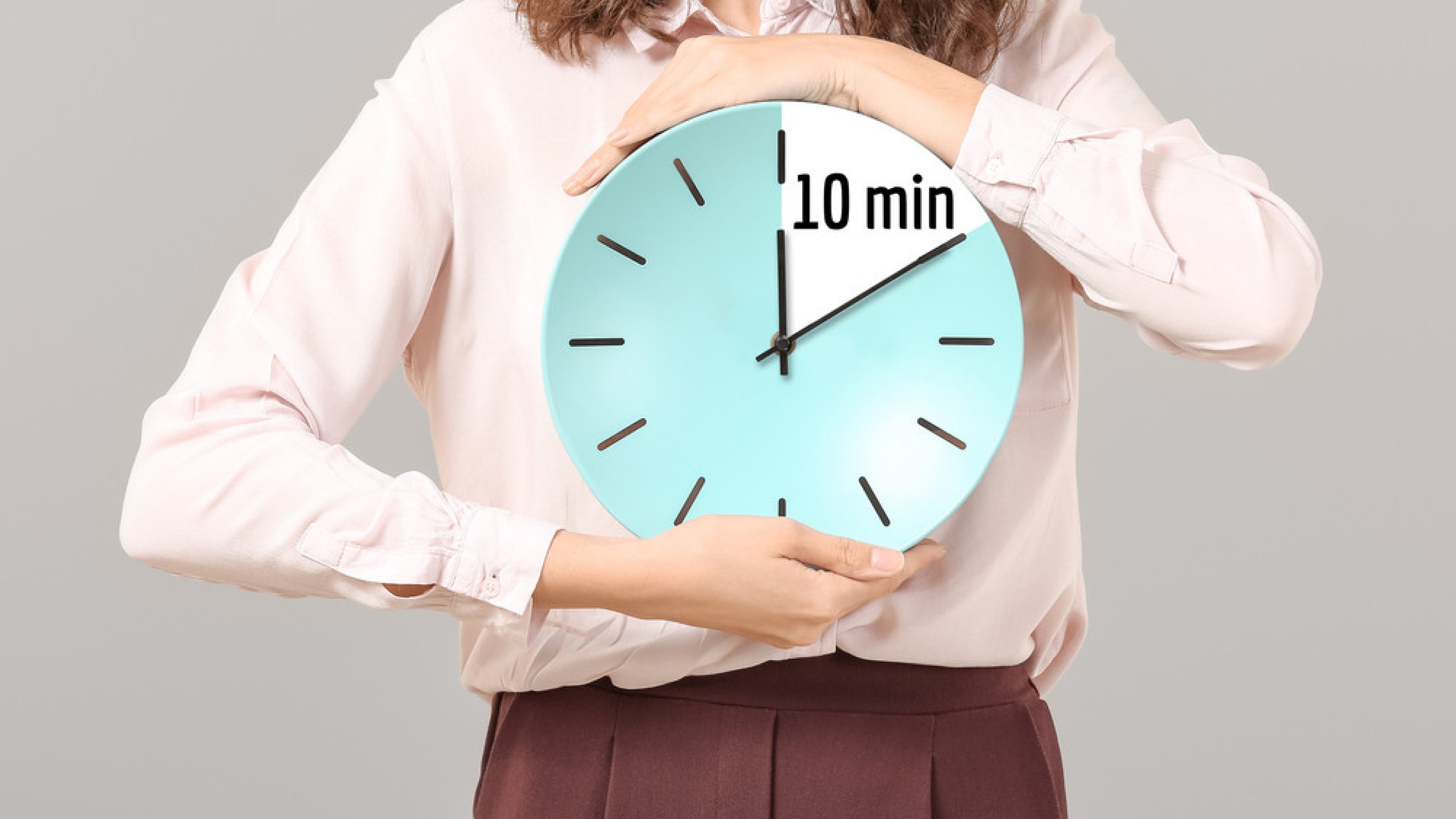 Businesswoman holding clock with timer for 10 minutes on grey background. Time management concept