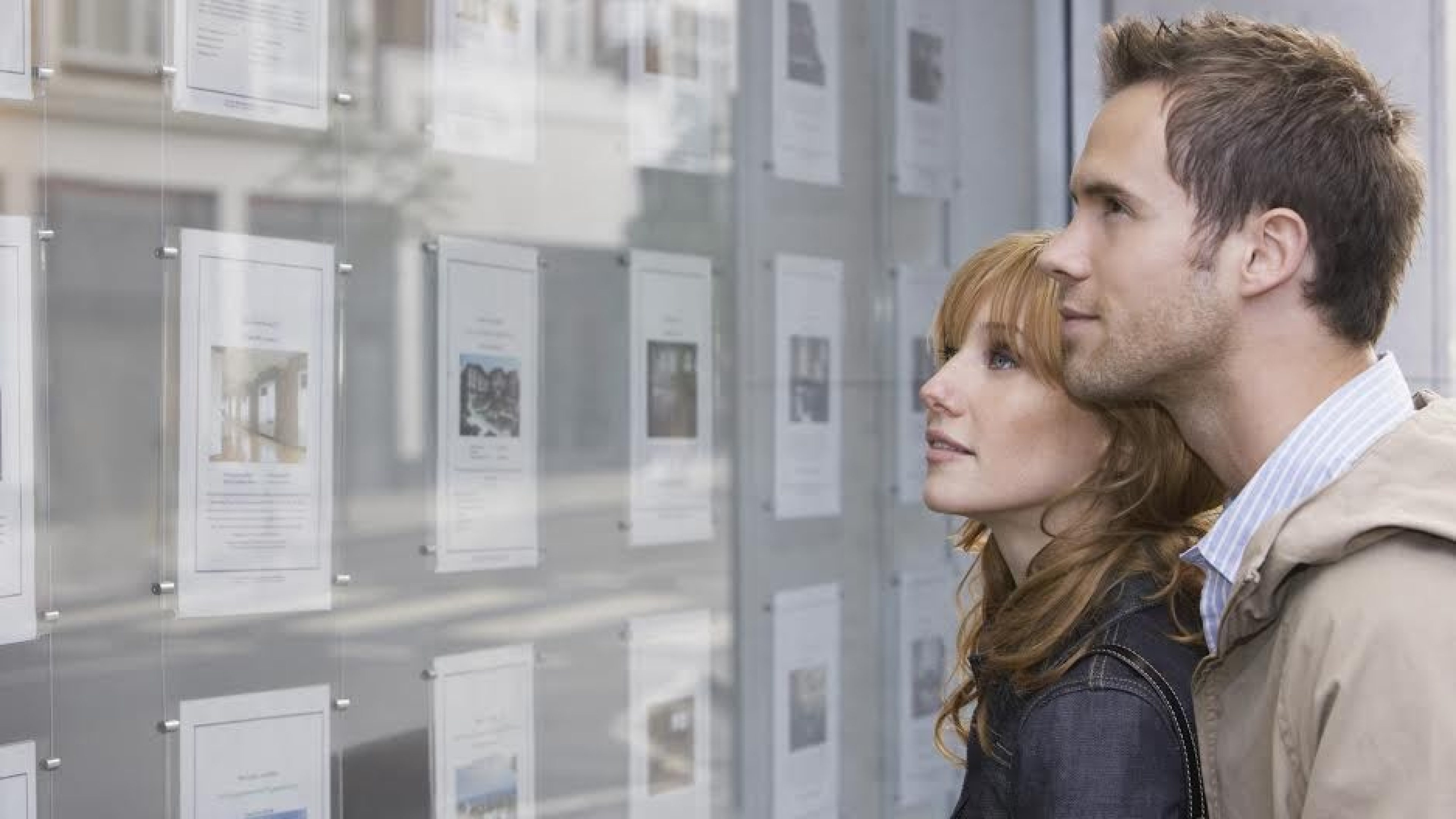 Side view of a young couple looking at window display at real estate office