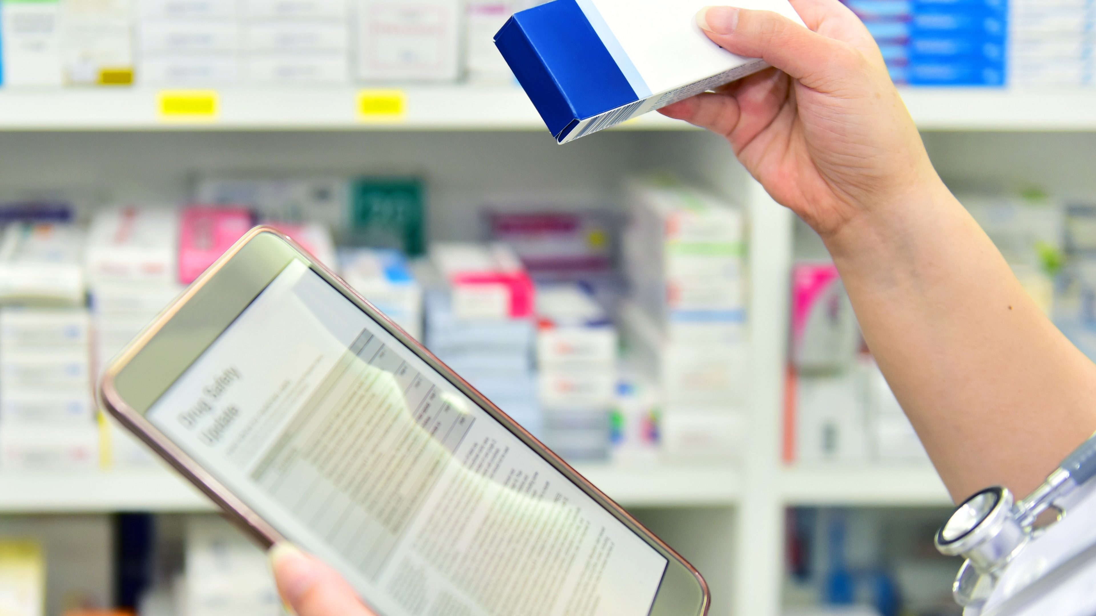 Doctor holding medicine box and computer tablet for filling prescription in pharmacy drugstore.