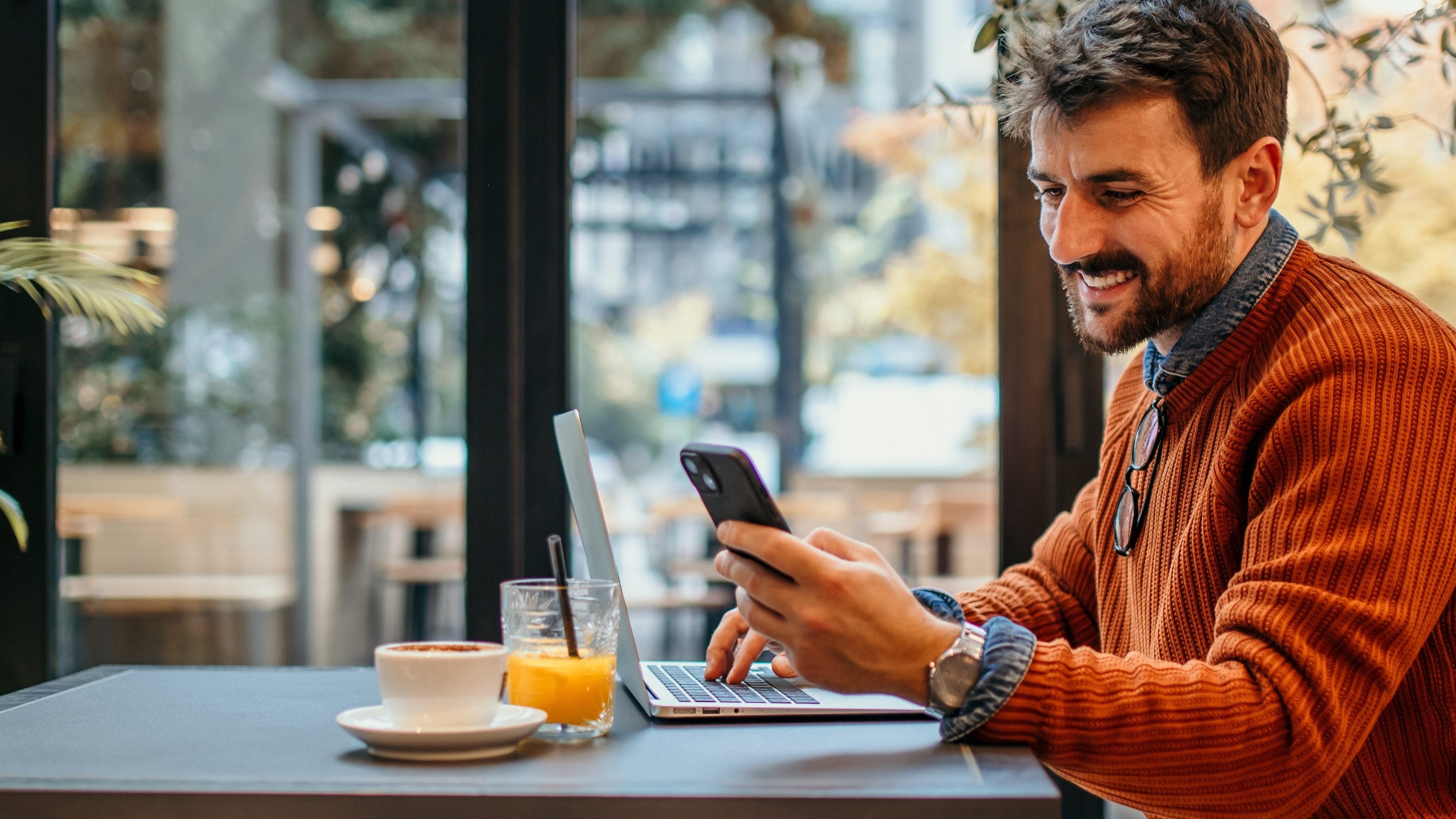 Handsome Caucasian man using a phone in the cafe and working on the laptop. Freelancer. Online work concept