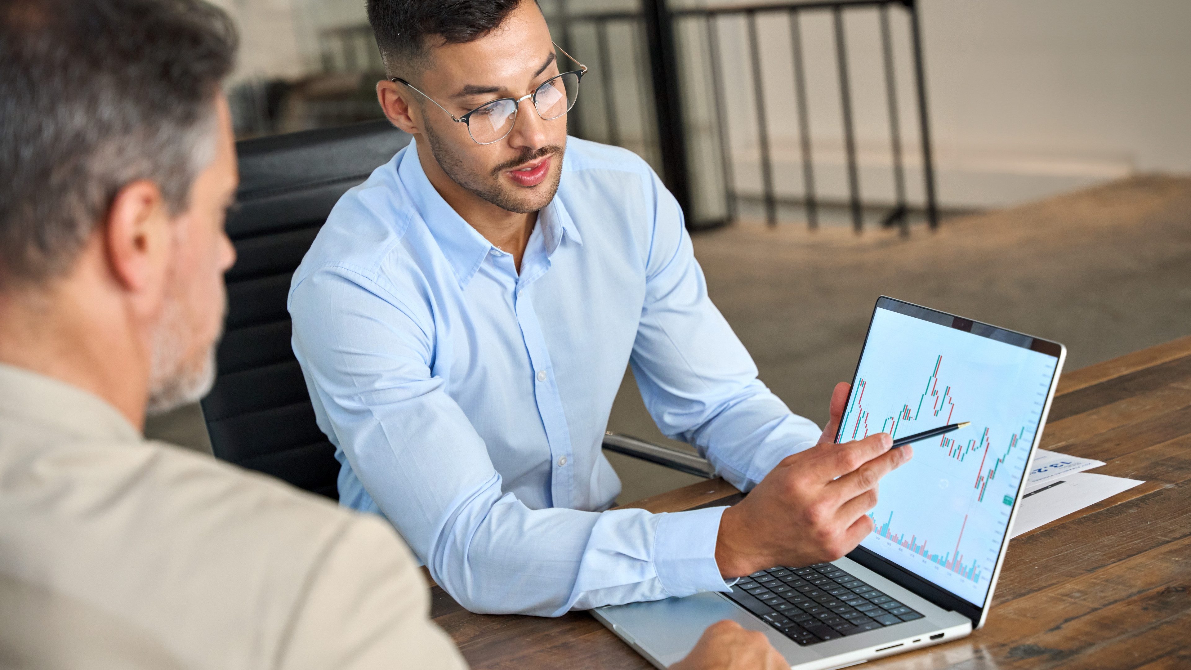 Financial advisor explaining invest stock market data consulting investor. Two busy business men analysts doing finance trading analysis pointing at exchange chart on laptop screen working in office.